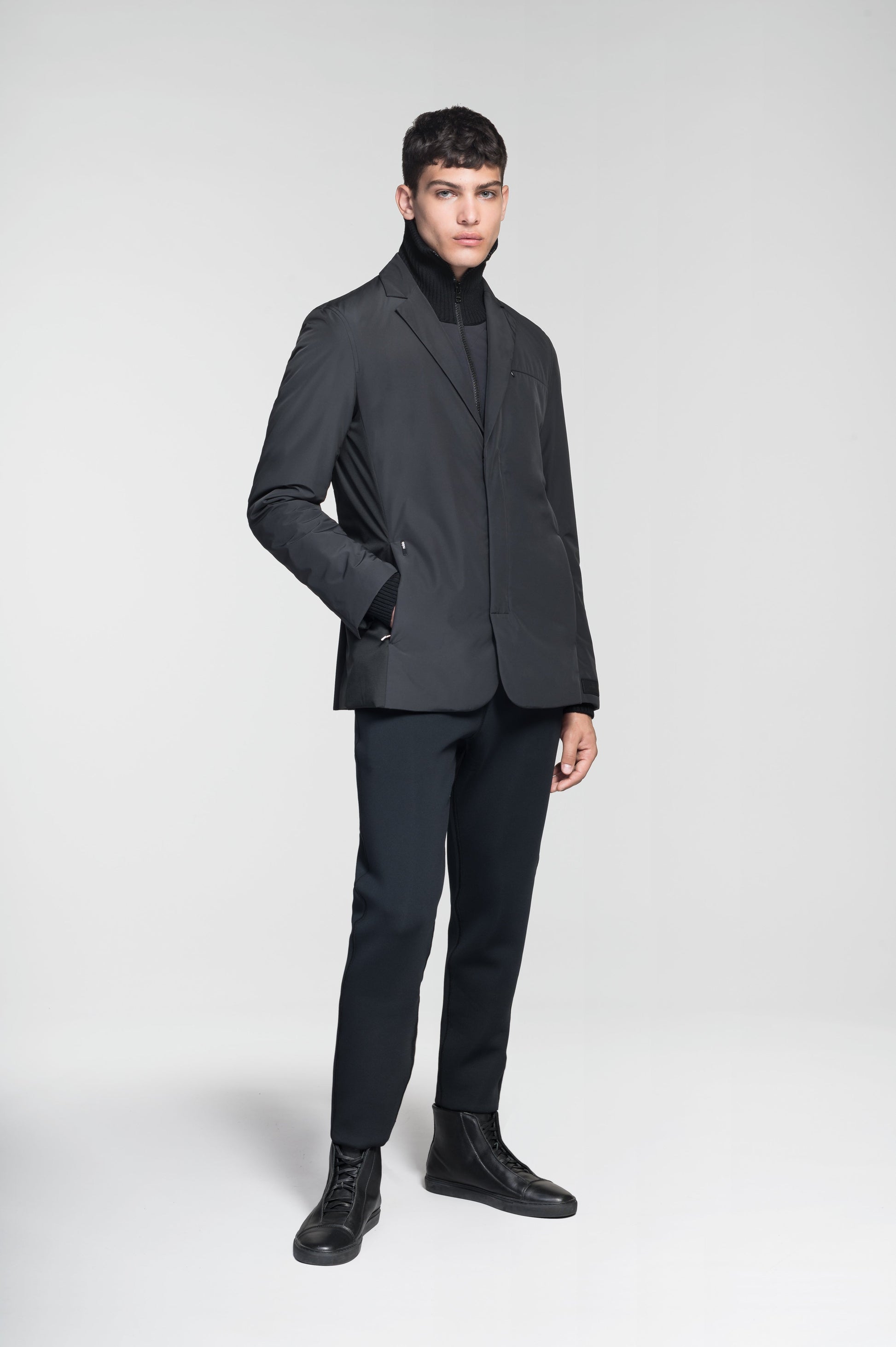 Cody Men's Tailored Travel Blazer in 3-ply micro denier and stretch nylon fabrication with DWR coating, Primaloft Gold Insulation Active+, hidden two-way zipper at centre front with snap closure placket, three invisible exterior zipper pockets, double back pleats, and hidden snap placket at cuffs, in Black