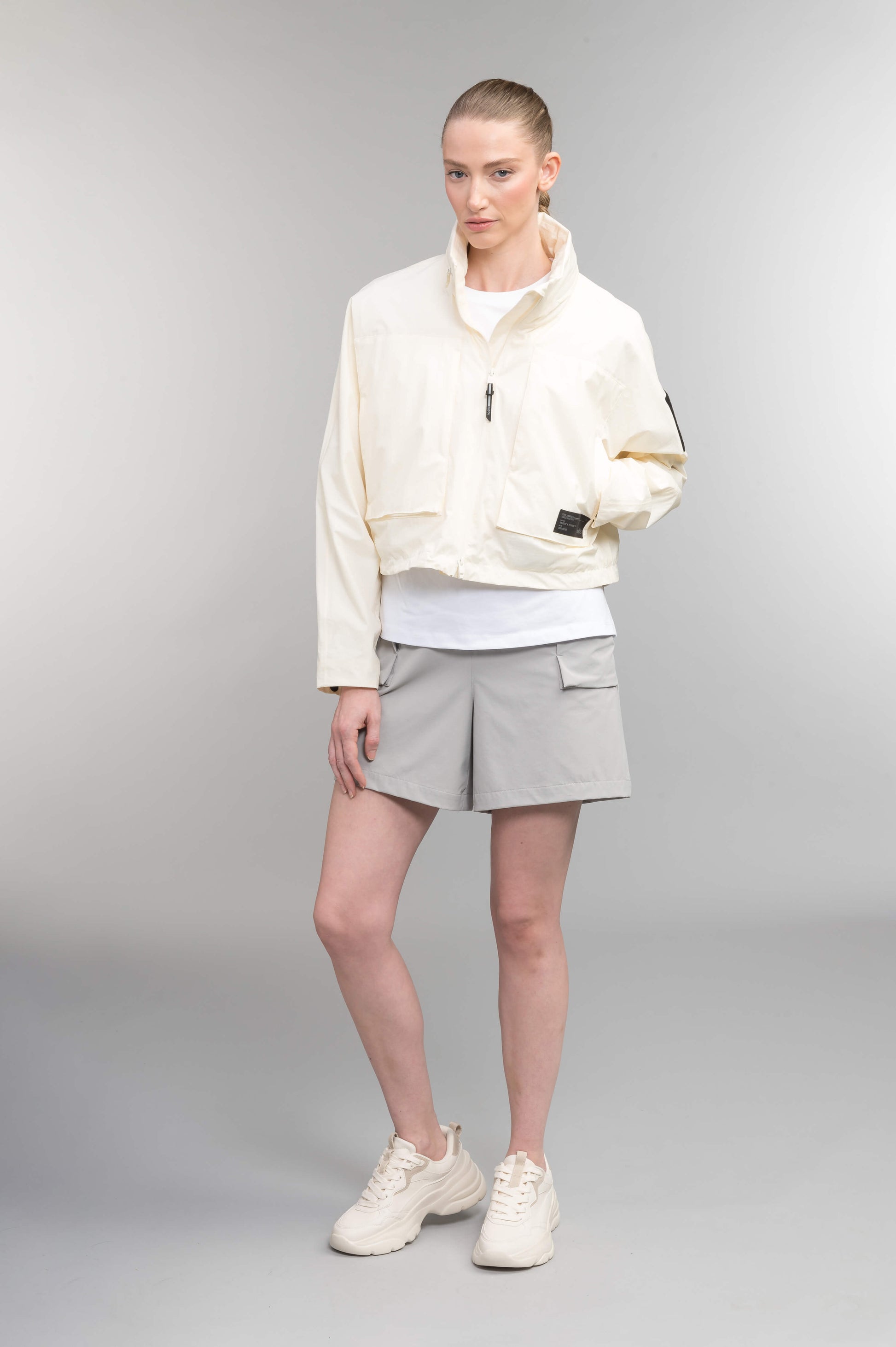 Epsie Women's Cropped Rain Jacket in Chalk crafted from premium recycled polyester ripstop with a DWR coating and taffeta nylon lining. Features a hidden packaway hood stored in the collar, two-way waterproof front zipper, seam-sealed construction, underarm zip ventilation, adjustable drawcord hem, zippered waist patch pockets, and an interior chest pocket for secure storage. Machine washable. Designed in Canada.
