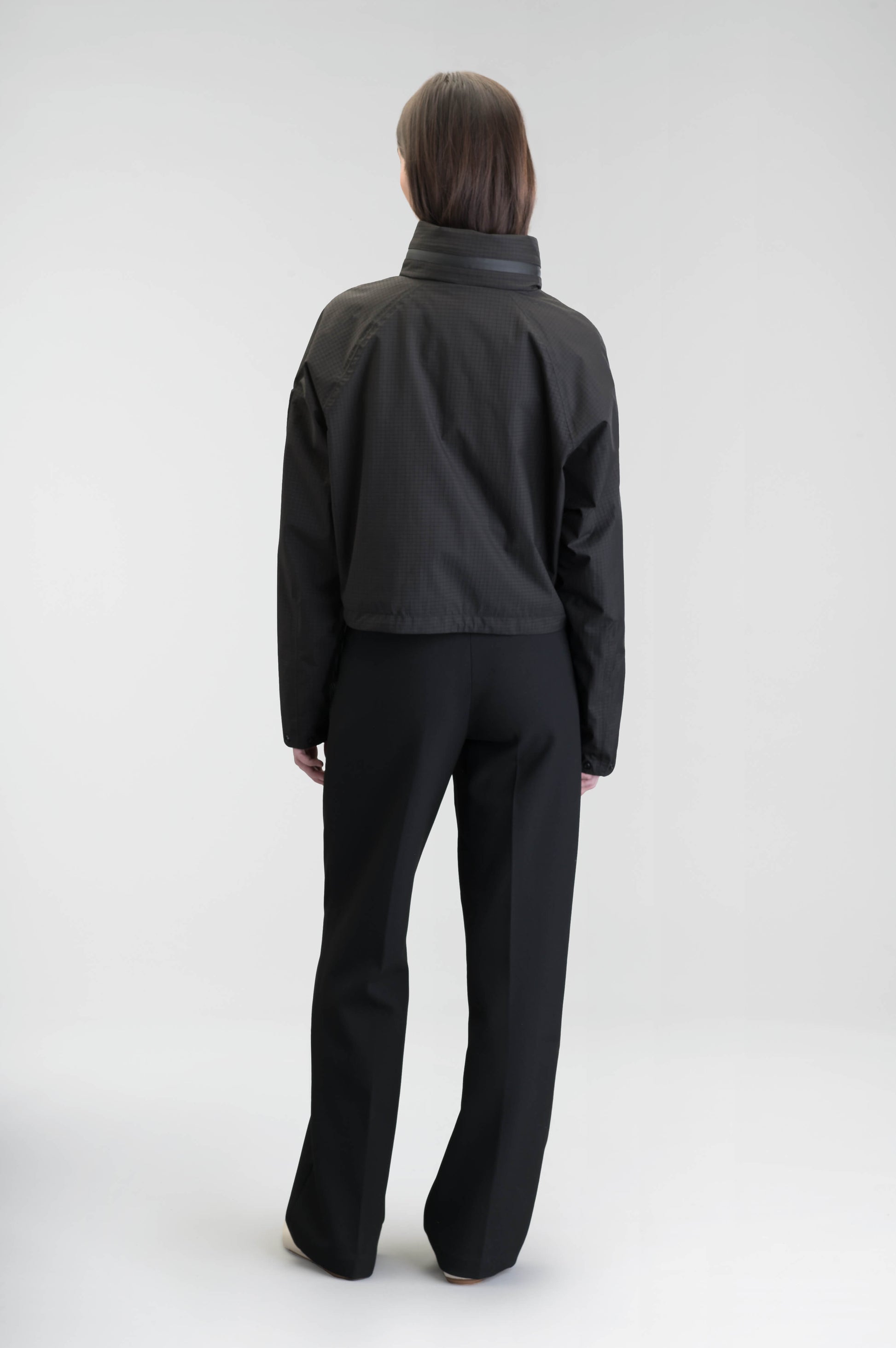 Epsie Women's Cropped Rain Jacket in Black crafted from premium recycled polyester ripstop with a DWR coating and taffeta nylon lining. Features a hidden packaway hood stored in the collar, two-way waterproof front zipper, seam-sealed construction, underarm zip ventilation, adjustable drawcord hem, zippered waist patch pockets, and an interior chest pocket for secure storage. Machine washable. Designed in Canada.