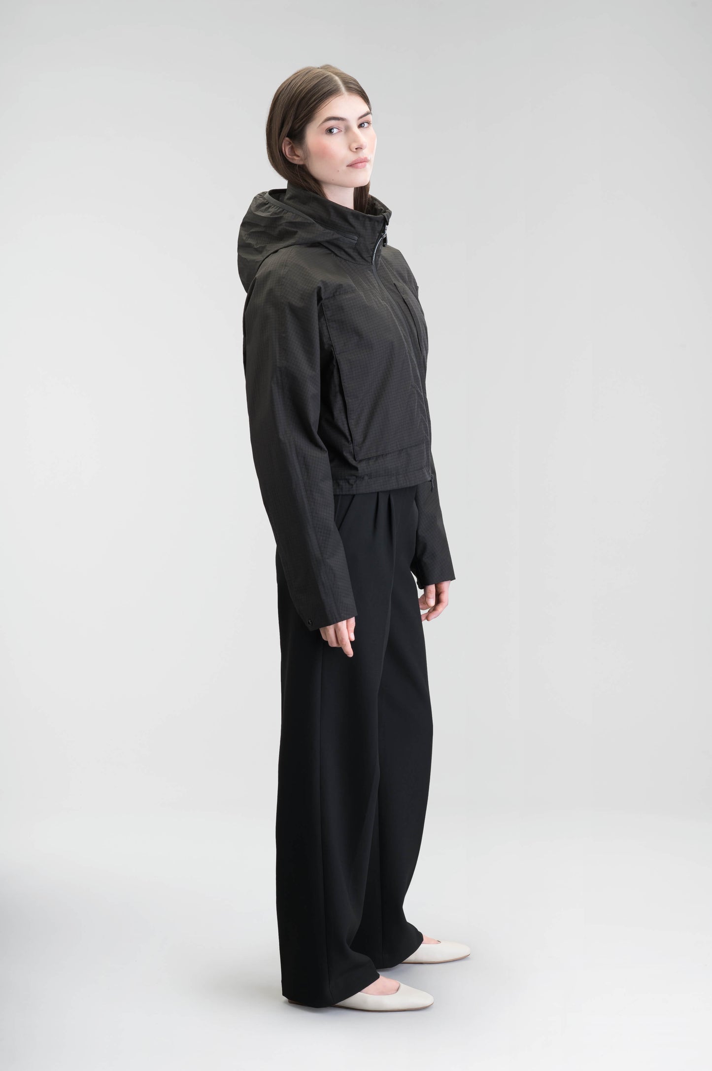 Epsie Women's Cropped Rain Jacket in Black crafted from premium recycled polyester ripstop with a DWR coating and taffeta nylon lining. Features a hidden packaway hood stored in the collar, two-way waterproof front zipper, seam-sealed construction, underarm zip ventilation, adjustable drawcord hem, zippered waist patch pockets, and an interior chest pocket for secure storage. Machine washable. Designed in Canada.