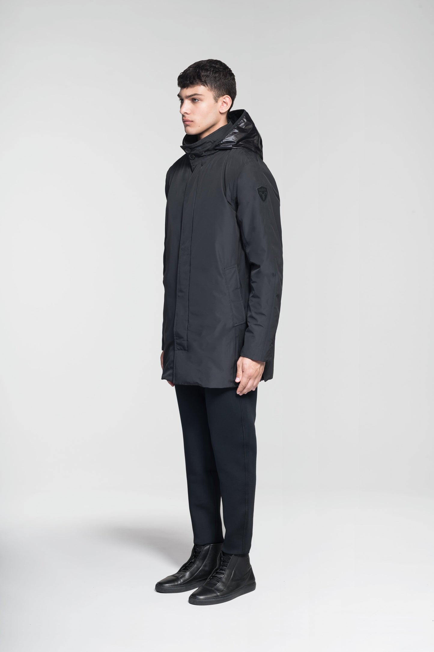 Pike Men's Tailored Mac Coat in thigh length, premium 3-ply Micro Denier fabrication at body and cire technical nylon taffeta fabrication at hood, premium 4-way stretch, water resistant Primaloft Gold Insulation Active+, hidden 2-way zipper with snap closure wind flap, single welt pockets with magnetic closure at waist, hidden snap placket at cuffs, pit zippers for ventilation, interior zipper pocket at right chest, and interior button pocket at left chest, in Black