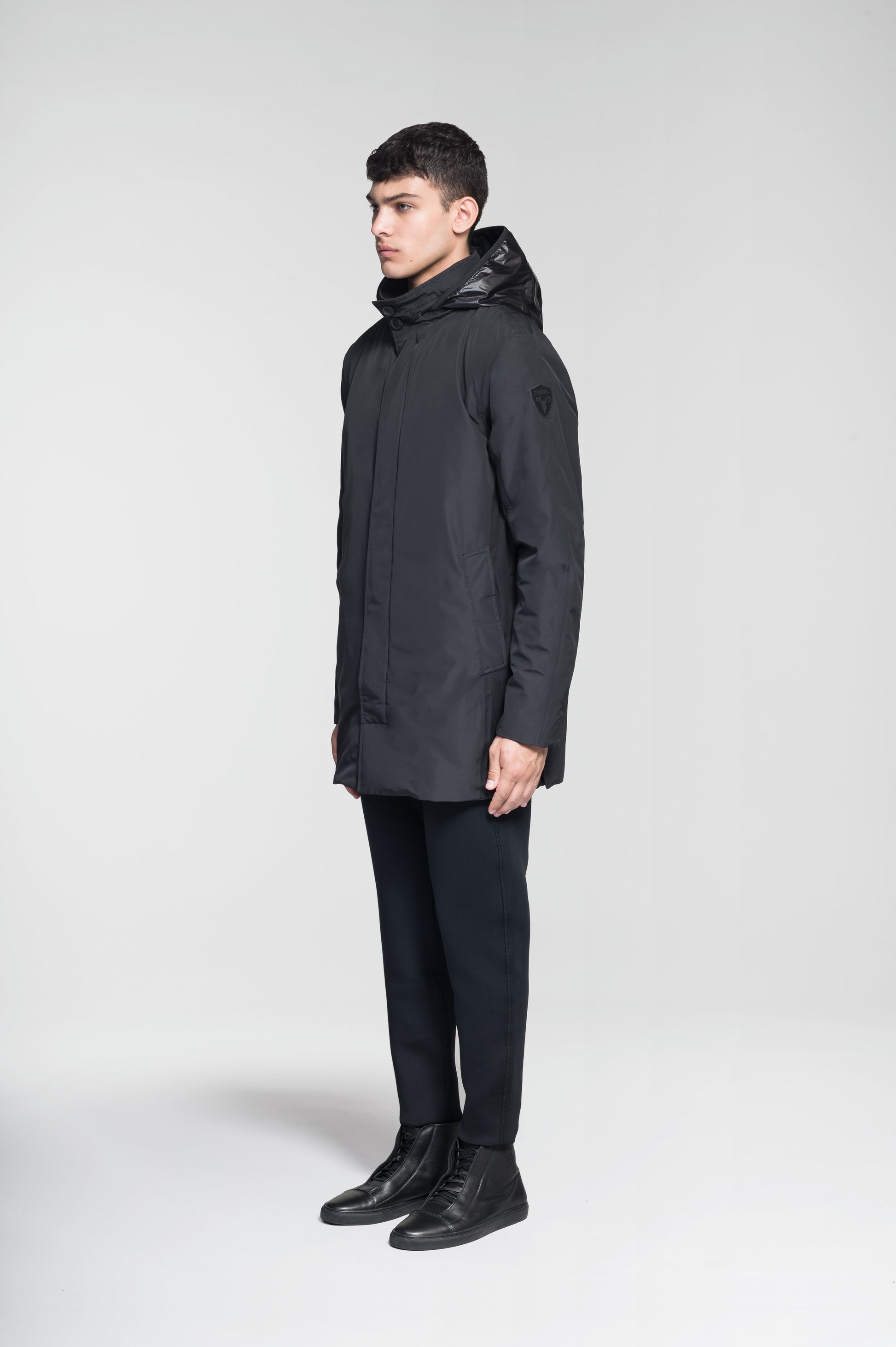 Pike Men's Tailored Mac Coat in thigh length, premium 3-ply Micro Denier fabrication at body and cire technical nylon taffeta fabrication at hood, premium 4-way stretch, water resistant Primaloft Gold Insulation Active+, hidden 2-way zipper with snap closure wind flap, single welt pockets with magnetic closure at waist, hidden snap placket at cuffs, pit zippers for ventilation, interior zipper pocket at right chest, and interior button pocket at left chest, in Black