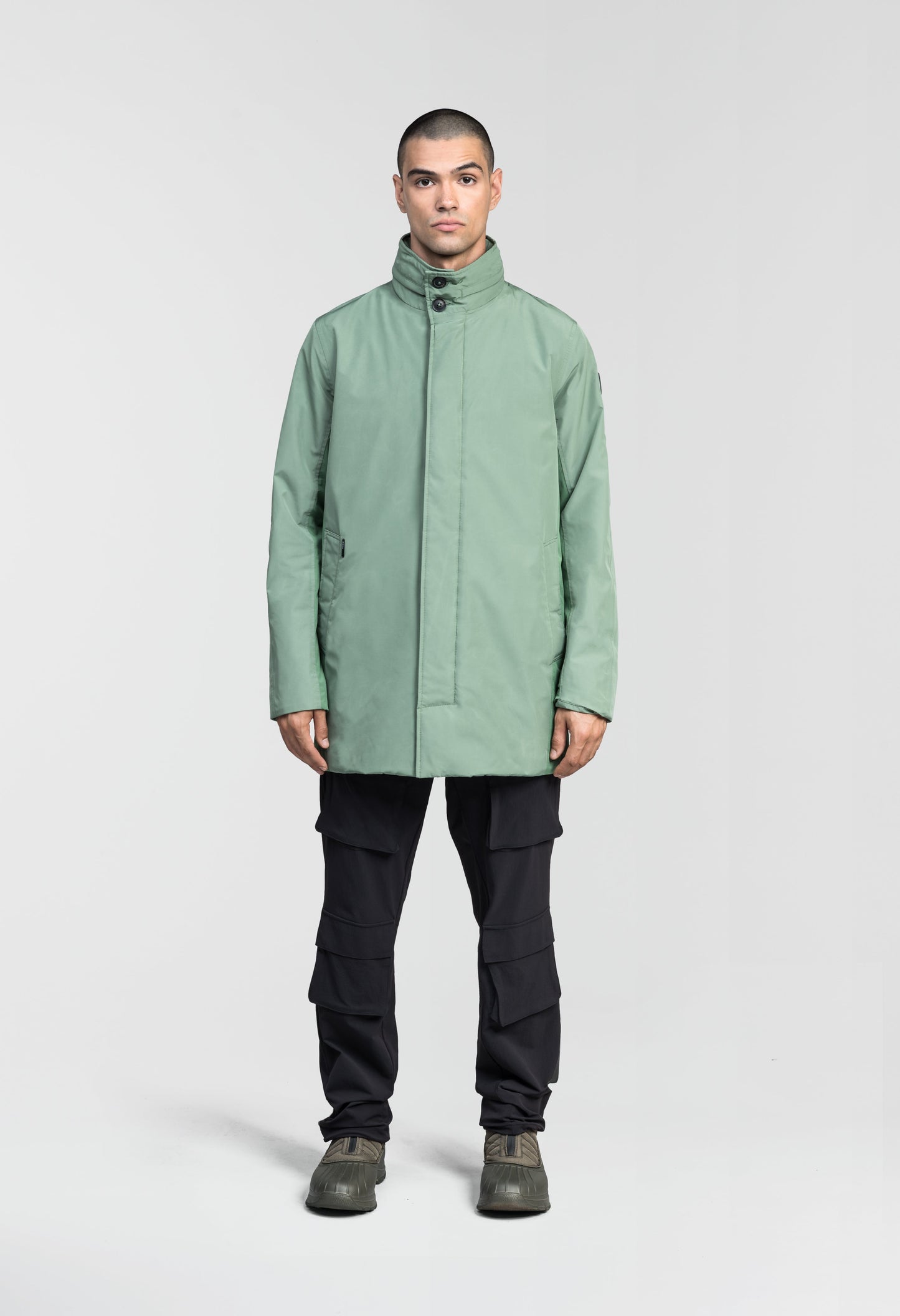 Pike Men's Tailored Mac Coat in thigh length, premium 3-ply Micro Denier fabrication at body and cire technical nylon taffeta fabrication at hood, premium 4-way stretch, water resistant Primaloft Gold Insulation Active+, hidden 2-way zipper with snap closure wind flap, single welt pockets with magnetic closure at waist, hidden snap placket at cuffs, pit zippers for ventilation, interior zipper pocket at right chest, and interior button pocket at left chest, in Comfrey