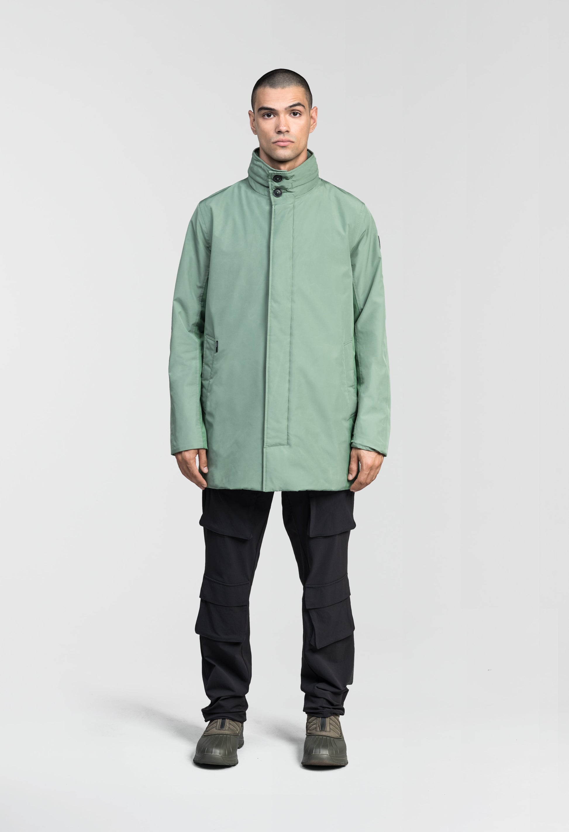Pike Men's Tailored Mac Coat in thigh length, premium 3-ply Micro Denier fabrication at body and cire technical nylon taffeta fabrication at hood, premium 4-way stretch, water resistant Primaloft Gold Insulation Active+, hidden 2-way zipper with snap closure wind flap, single welt pockets with magnetic closure at waist, hidden snap placket at cuffs, pit zippers for ventilation, interior zipper pocket at right chest, and interior button pocket at left chest, in Comfrey