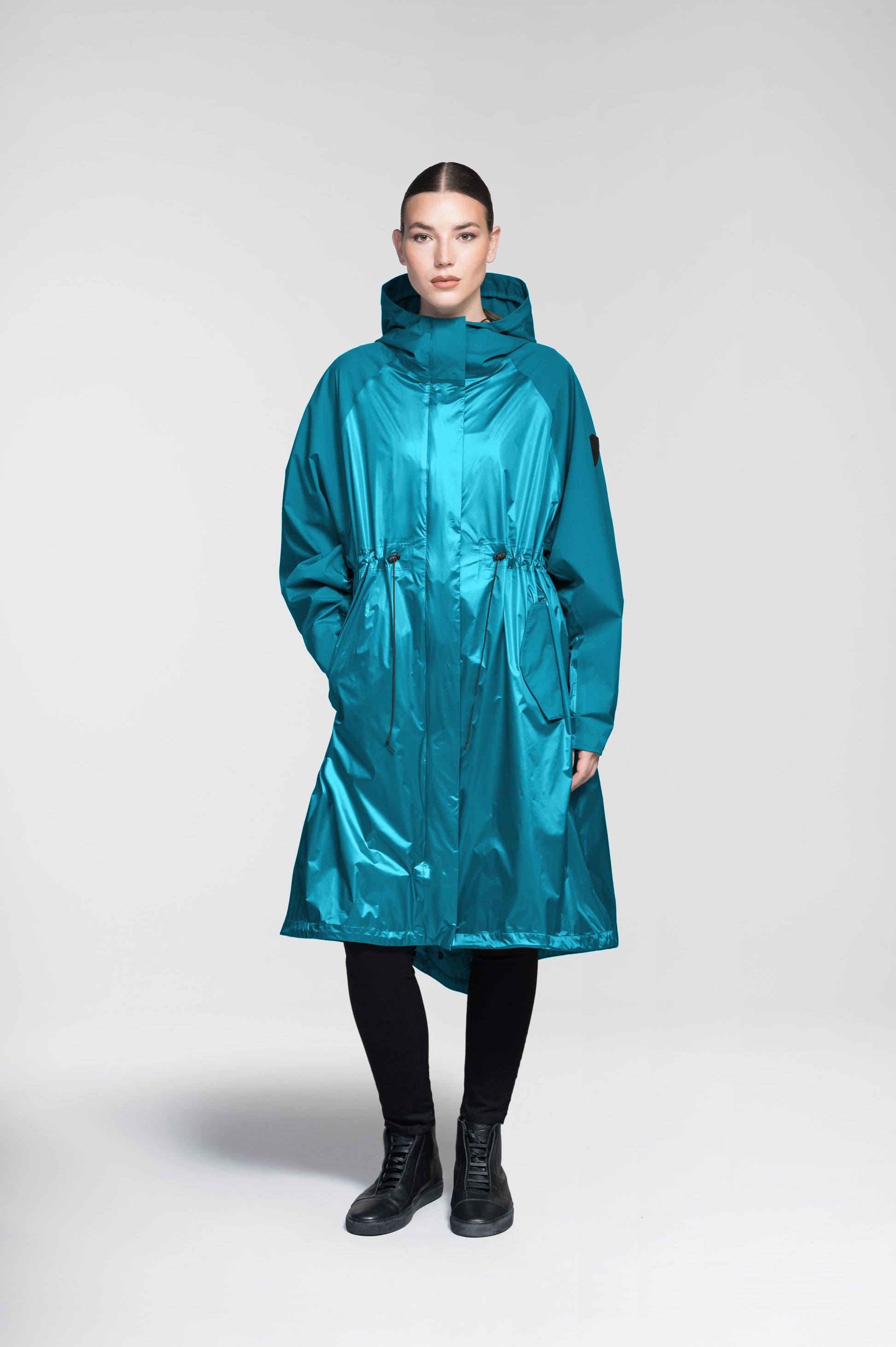 Reyna Women's Tailored Packable Long Shell Jacket in knee length, premium strech ripstop and contrast cire technical nylon taffeta fabrication, non-removable hood with adjustable draw cord, waist flap pockets with magnetic closures, adjustable draw cords at waist and bottom hem, adjustable snap cuffs, mesh back ventilation, hidden packable pocket, snap button wind flap, two-way branded zipper at centre front, adjustable snap button fishtail yoke at back, and large interior zipper pocket, in Deep Lake