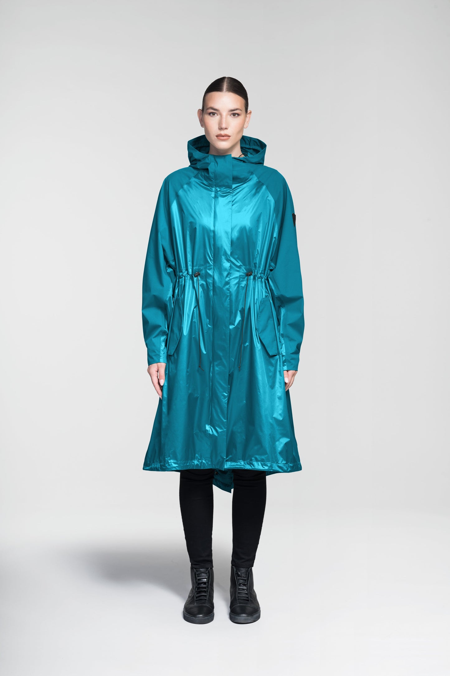 Reyna Women's Tailored Packable Long Shell Jacket in knee length, premium strech ripstop and contrast cire technical nylon taffeta fabrication, non-removable hood with adjustable draw cord, waist flap pockets with magnetic closures, adjustable draw cords at waist and bottom hem, adjustable snap cuffs, mesh back ventilation, hidden packable pocket, snap button wind flap, two-way branded zipper at centre front, adjustable snap button fishtail yoke at back, and large interior zipper pocket, in Deep Lake