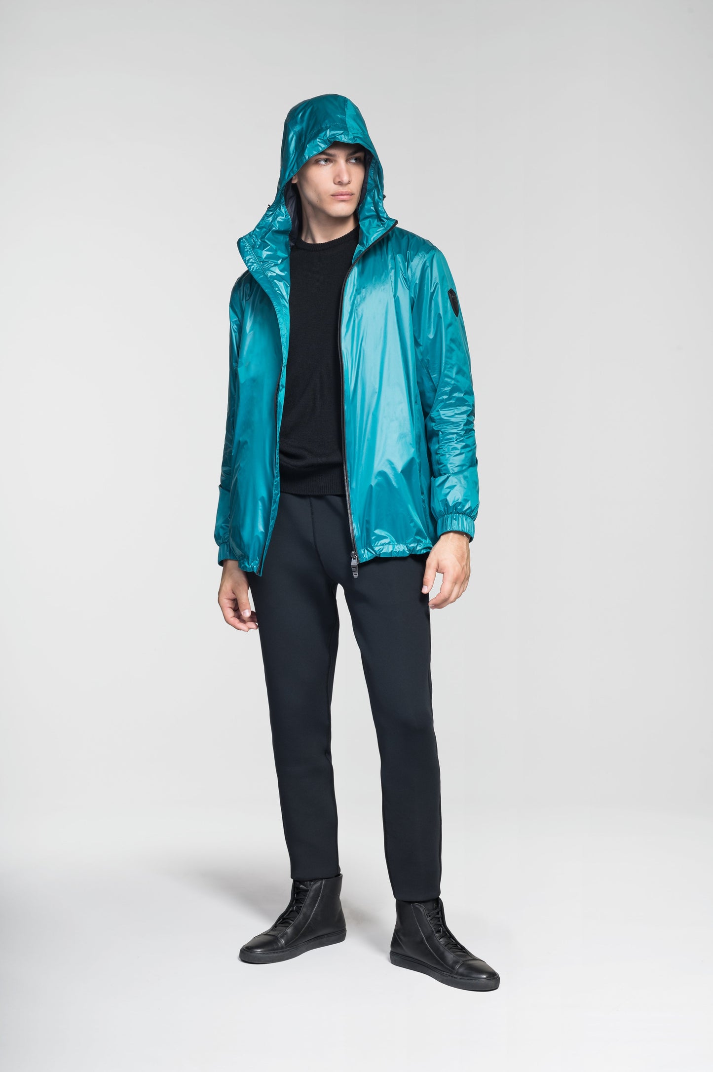 Stratus Men's Tailored Packable Rain Jacket in hip length, premium cire technical nylon taffeta and stretch ripstop fabrication, highly breathable mesh lining, hidden packable pocket, non-removable hood with adjustable draw cord, reflective piping along front and back, underarm grommets for extra breathability, back yoke with mesh ventilation, two waist zipper pockets, two interior zipper pockets, elastic cuffs with adjustable snap button, and adjustable interior draw cord at waist hem, in Deep Lake