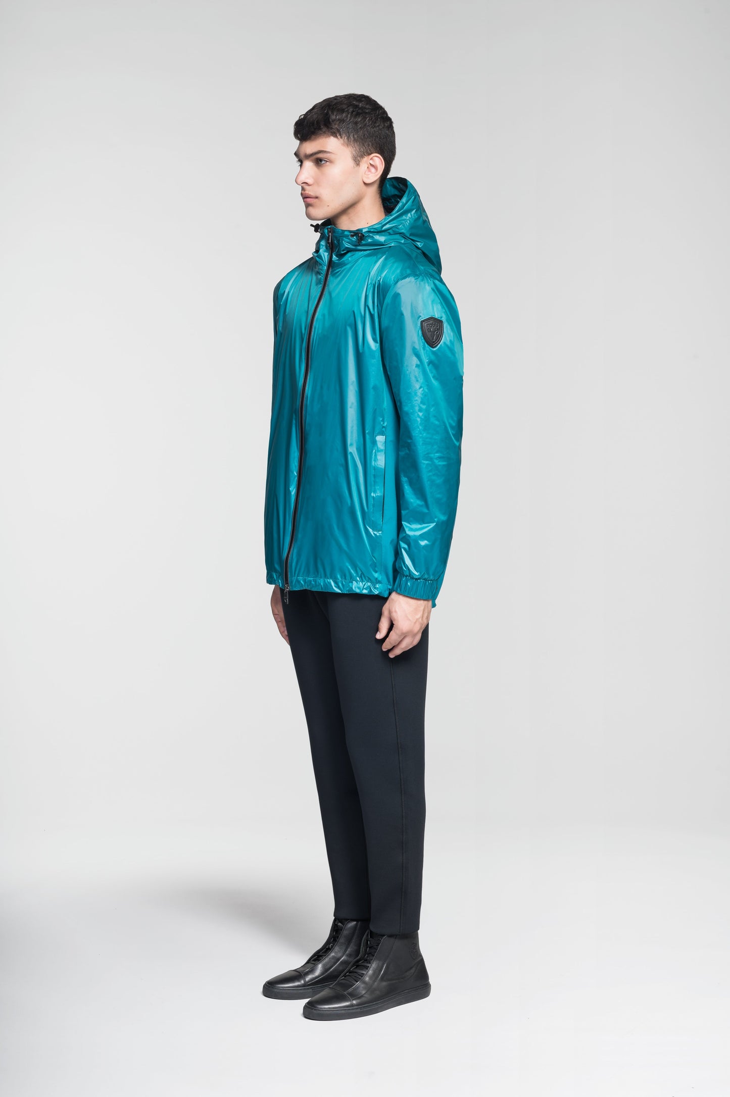 Stratus Men's Tailored Packable Rain Jacket in hip length, premium cire technical nylon taffeta and stretch ripstop fabrication, highly breathable mesh lining, hidden packable pocket, non-removable hood with adjustable draw cord, reflective piping along front and back, underarm grommets for extra breathability, back yoke with mesh ventilation, two waist zipper pockets, two interior zipper pockets, elastic cuffs with adjustable snap button, and adjustable interior draw cord at waist hem, in Deep Lake