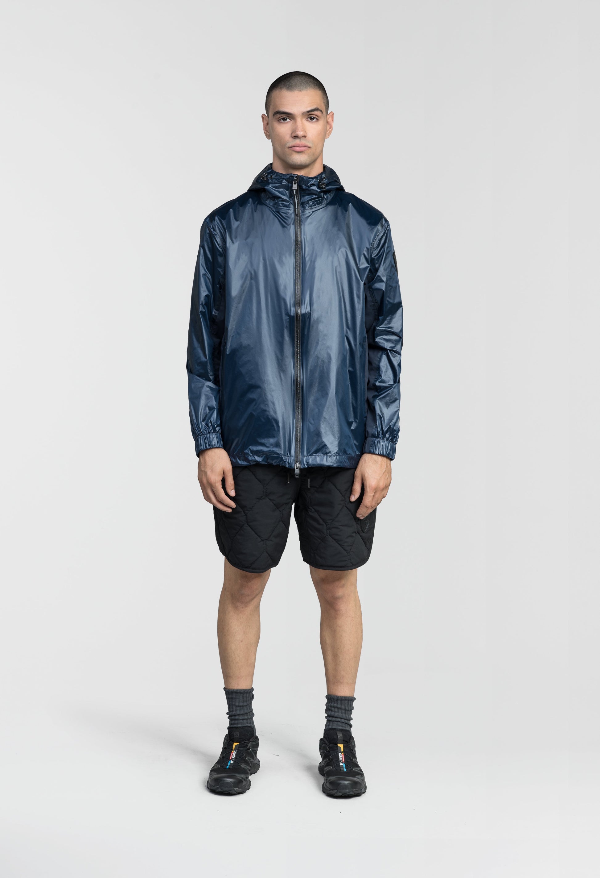 Stratus Men's Tailored Packable Rain Jacket in hip length, premium cire technical nylon taffeta and stretch ripstop fabrication, highly breathable mesh lining, hidden packable pocket, non-removable hood with adjustable draw cord, reflective piping along front and back, underarm grommets for extra breathability, back yoke with mesh ventilation, two waist zipper pockets, two interior zipper pockets, elastic cuffs with adjustable snap button, and adjustable interior draw cord at waist hem, in Marine