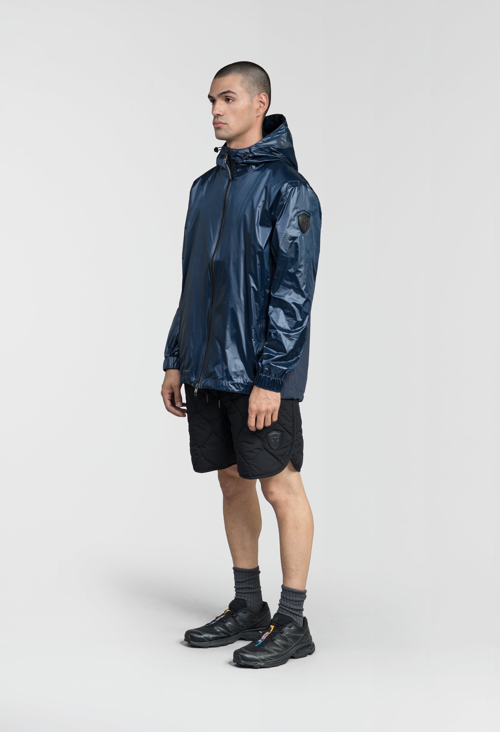 Stratus Men's Tailored Packable Rain Jacket in hip length, premium cire technical nylon taffeta and stretch ripstop fabrication, highly breathable mesh lining, hidden packable pocket, non-removable hood with adjustable draw cord, reflective piping along front and back, underarm grommets for extra breathability, back yoke with mesh ventilation, two waist zipper pockets, two interior zipper pockets, elastic cuffs with adjustable snap button, and adjustable interior draw cord at waist hem, in Marine