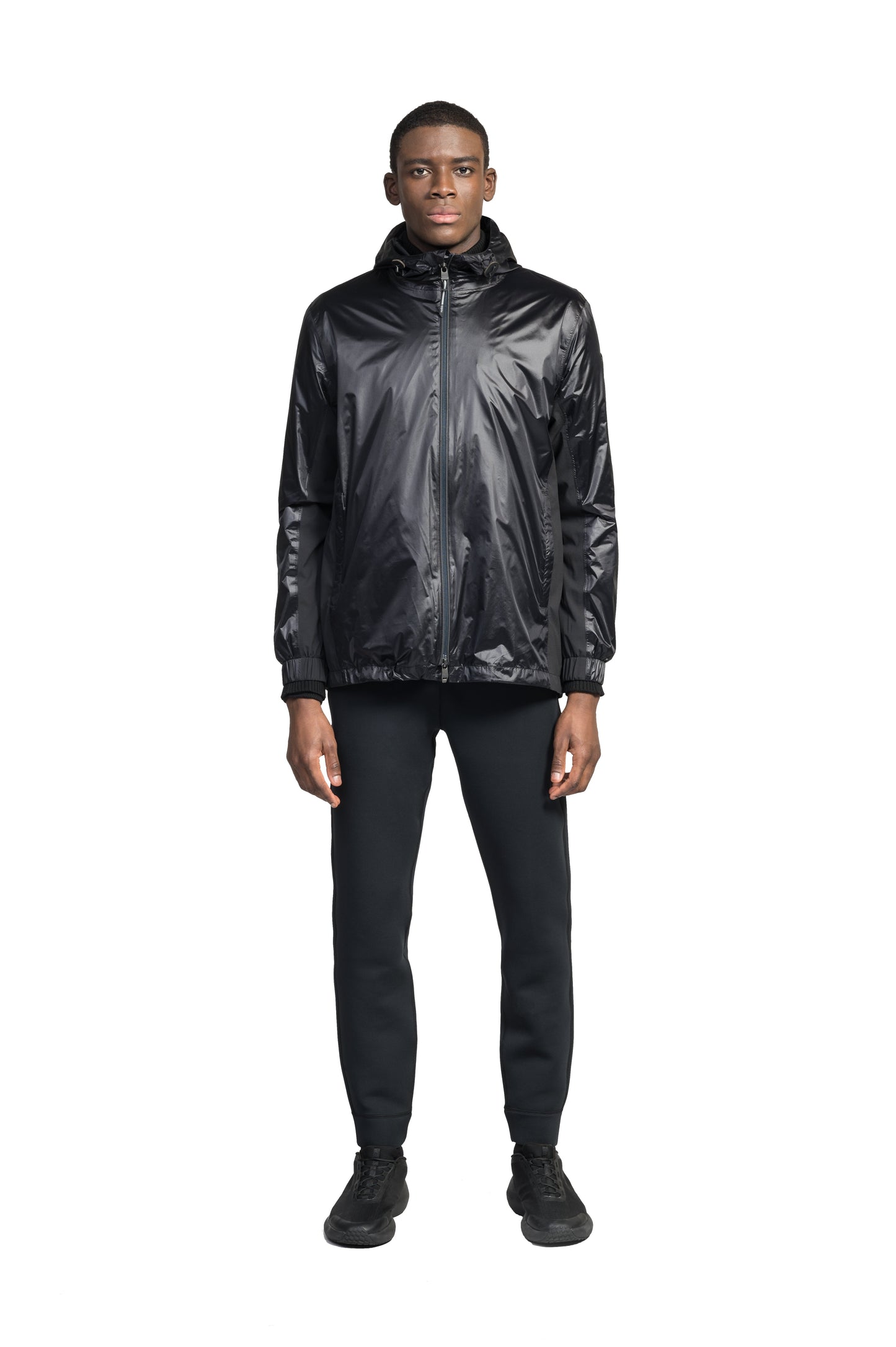 Stratus Men's Tailored Packable Rain Jacket in hip length, premium cire technical nylon taffeta and stretch ripstop fabrication, highly breathable mesh lining, hidden packable pocket, non-removable hood with adjustable draw cord, reflective piping along front and back, underarm grommets for extra breathability, back yoke with mesh ventilation, two waist zipper pockets, two interior zipper pockets, elastic cuffs with adjustable snap button, and adjustable interior draw cord at waist hem, in Black