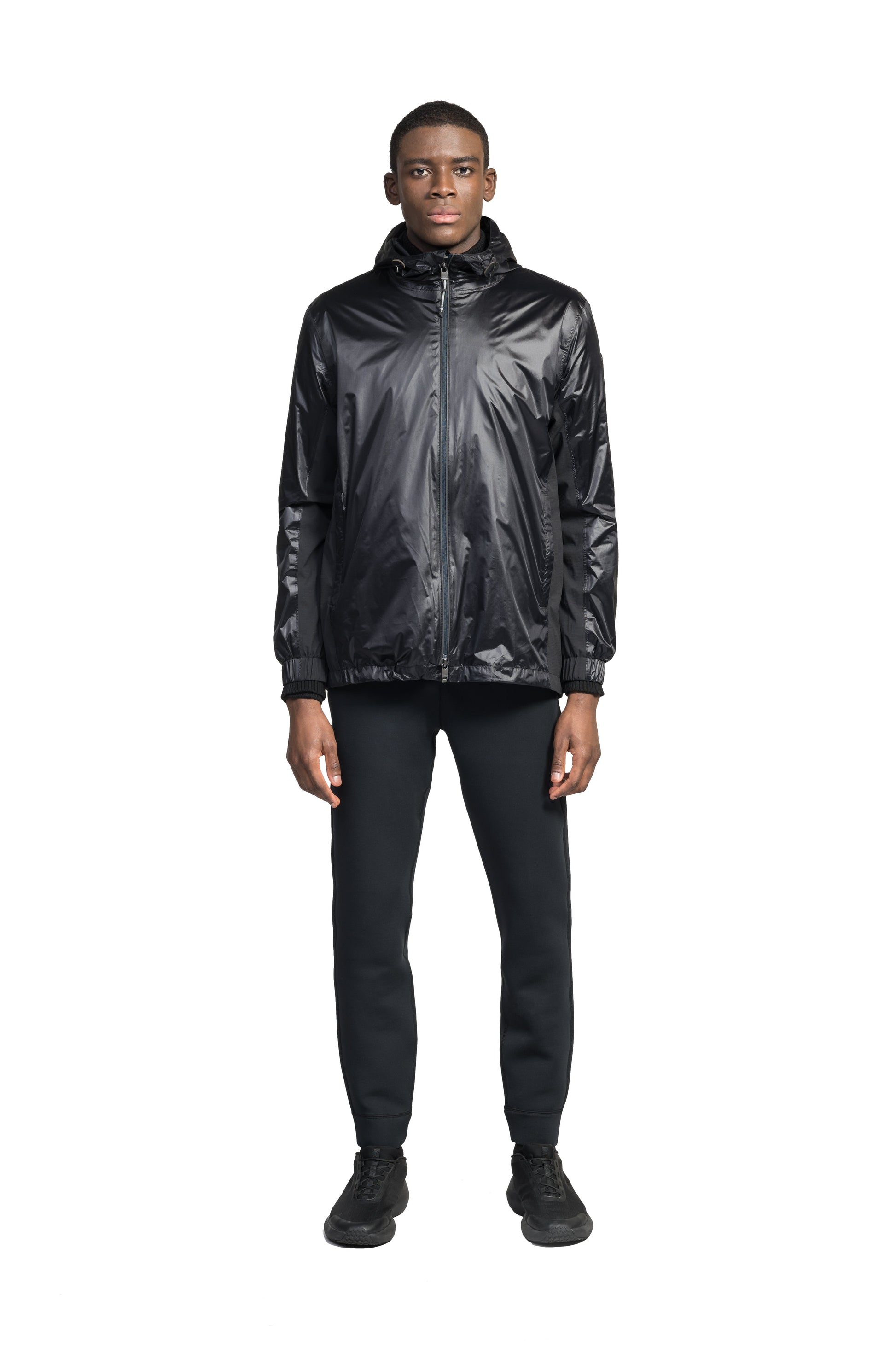 Stratus Men's Tailored Packable Rain Jacket in hip length, premium cire technical nylon taffeta and stretch ripstop fabrication, highly breathable mesh lining, hidden packable pocket, non-removable hood with adjustable draw cord, reflective piping along front and back, underarm grommets for extra breathability, back yoke with mesh ventilation, two waist zipper pockets, two interior zipper pockets, elastic cuffs with adjustable snap button, and adjustable interior draw cord at waist hem, in Black