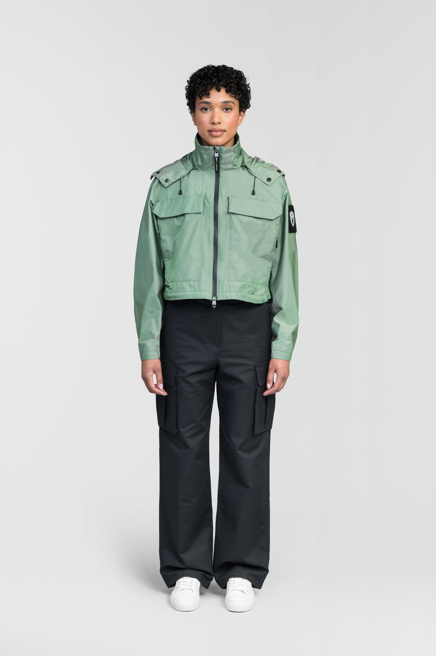 Viva Women's Performance Cropped Jacket in waist length, premium iridescent fabrication, removable hood with peak, adjustable hood draw cords and toggle, 2-way branded zipper at centre front, oversized magnetic closure flap pockets at chest with side entry, interior adjustable draw cord at hem, large interior zipper pocket, and adjustable snap cuffs, in Comfrey