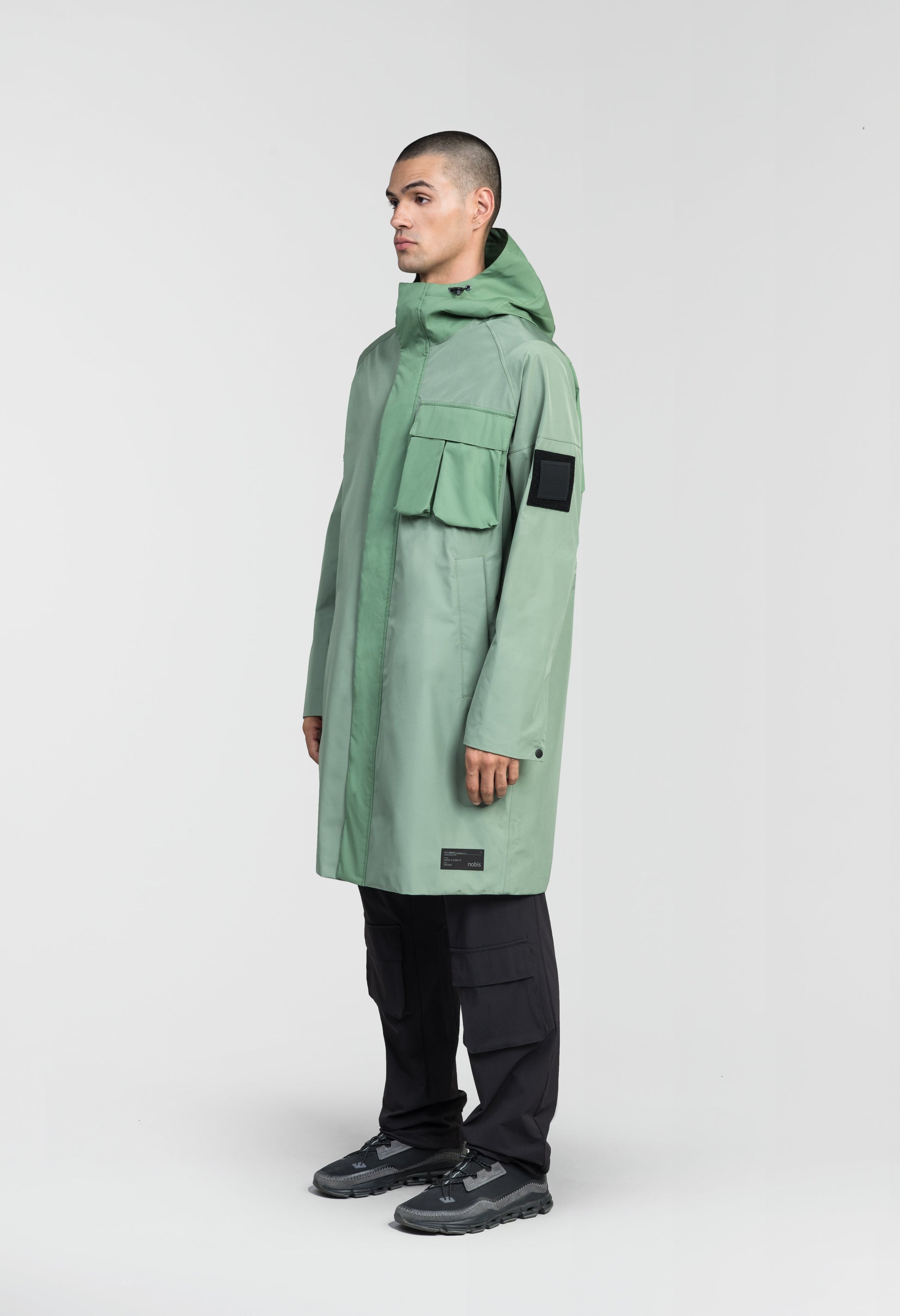 Wylder Men's Performance Rain Jacket in knee length, premium 3-ply Micro Denier and stretch ripstop fabrication, non-removable hood with reflective piping and adjustable draw cord, split utility chest pocket with magnetic flap closure, single welt pockets with magnetic closure at waist, back yoke with mesh ventilation, snap button wind flap, two-way branded zipper at centre front, telescopic sleeves with elasticized cuffs, interior draw cord at waist, in Comfrey